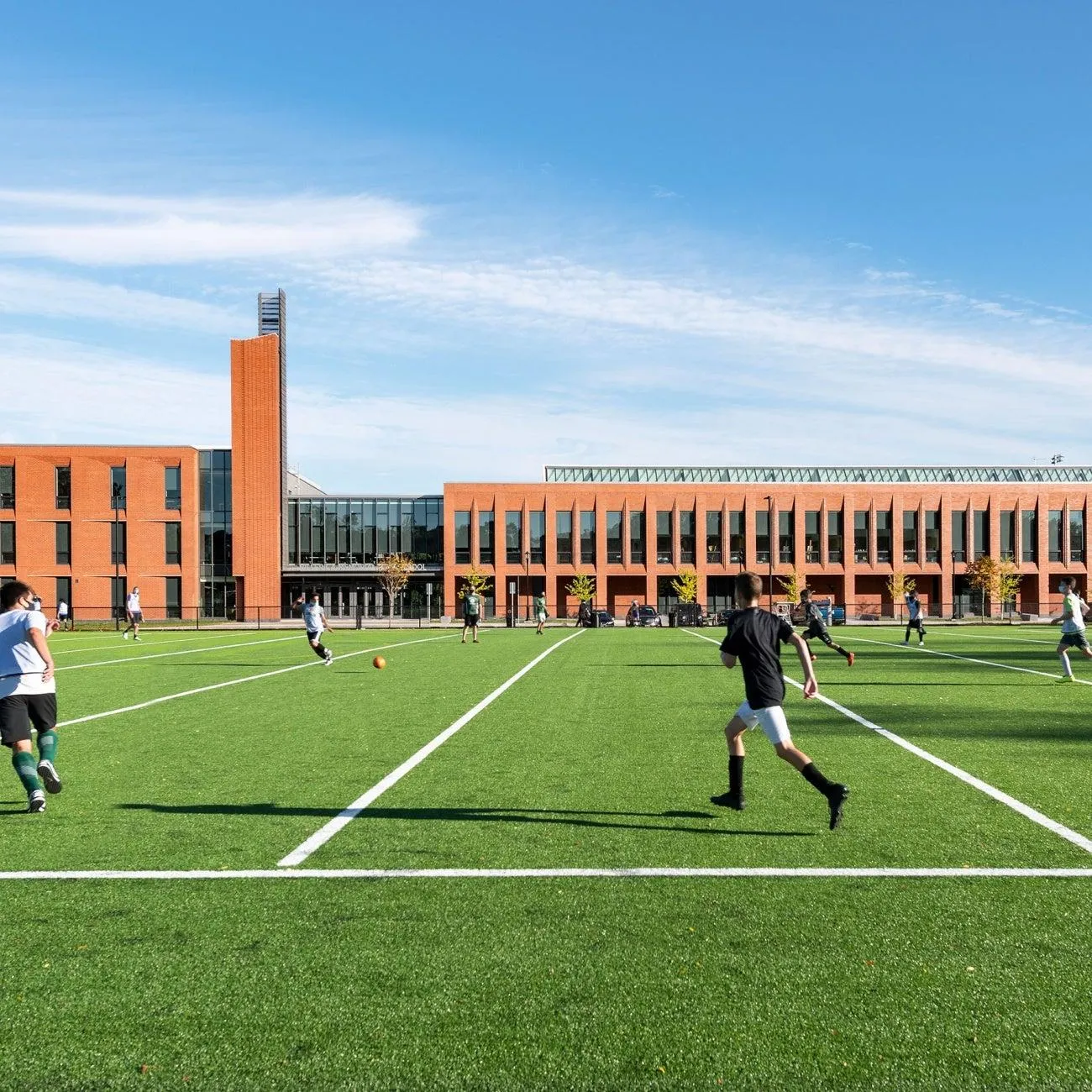 Students playing soccer on a school field in front of a large brick school building